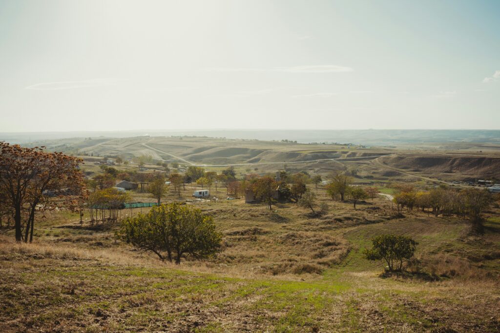 Expansive rural landscape with rolling hills and scattered farmhouses under a clear sky.